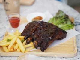 Pork Spareribs BBQ, Barbeque Pork Ribs with french fries vegetable salad, tomato sauce in a clear glass on wooden tray, food photo