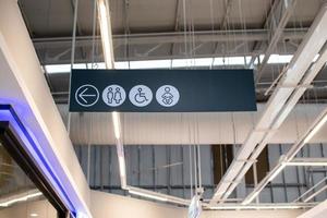 Sign to the bathroom on the left is a black and white symbol is hung to see. The sign contains arrow symbols to the left, women, men, disabled people, and children. Selective focus. Blurred background photo