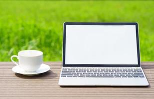 laptop and cofree cup on wood table agent grass field photo