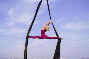 exercises with aerial silk outdoor, sky background. beautiful fit woman training acrobatic in airt. photo