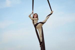 exercises with aerial silk outdoor, sky background. beautiful fit woman training acrobatic in airt. photo