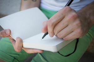 joven outddur en el parque escribe en un cuaderno, estudiante o escritor en el trabajo foto