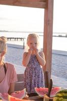 Mother with two kids eat watermelon slices outdoors in summertime photo