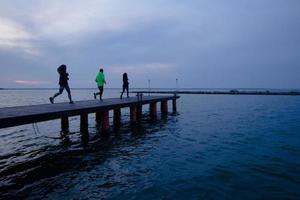 group of young people training outdoors, runners exercises, sea or river background photo