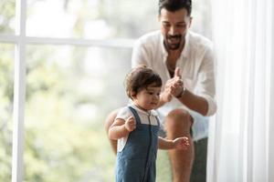 lindo concepto de familia de niño pequeño, bebé aprendiendo a caminar con el padre y la madre para ayudar a cuidar y tomar la mano, primer paso con el apoyo de los padres de la infancia, pequeño retrato de amor niño pequeño en casa foto