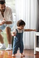 lindo concepto de familia de niño pequeño, bebé aprendiendo a caminar con el padre y la madre para ayudar a cuidar y tomar la mano, primer paso con el apoyo de los padres de la infancia, pequeño retrato de amor niño pequeño en casa foto