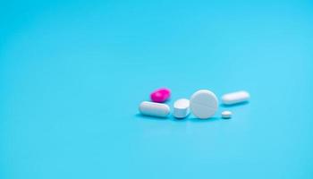 White tablets pills on blur pink tablet pill and blue background. Pharmacy banner. Pharmaceutical industry. Health insurance strategy. Prescription drugs. Polypharmacy and drug interactions problem. photo