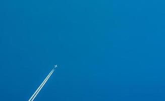 Airplane with white condensation tracks. Jet plane on clear blue sky with vapor trail. Travel by airplane concept. Trails of exhaust gas from airplane engine. Aircraft with white stripes. photo
