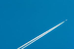 Airplane with white condensation tracks. Jet plane on clear blue sky with vapor trail. Travel by aeroplane concept. Trails of exhaust gas from airplane engine. Aircraft with white stripes. photo