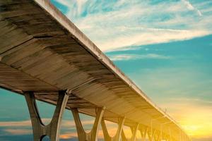 Bottom view of elevated concrete highway. Overpass concrete road. Road flyover structure. Modern motorway with golden sunrise sky. Concrete bridge engineering construction. Bridge architecture. photo