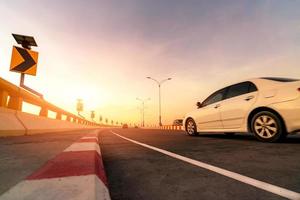 desenfoque de movimiento de la conducción de automóviles blancos en una carretera curva de hormigón con señal de tráfico. viaje por carretera en vacaciones de verano. unidad de coche en la calle. viajes de verano en coche. energía del panel solar en la señal de tráfico de la curva amarilla foto