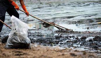 Volunteer use rake to sweep trash out of the sea. Beach cleaners collect garbage on the sea beach into transparent plastic bags. Volunteers cleaning beach. Tidying up rubbish on beach photo