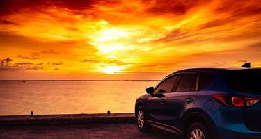 Blue compact SUV car with sport and modern design parked on concrete road by the sea at sunset. Hybrid auto and automotive concept. Road trip and car driving for travel. Car parked near the beach. photo