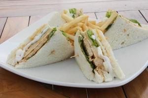 Triangular shaped sandwich. Stuffed thick meat, thin cheese, mayonnaise, lettuce. Pierced with a toothpick. On a white ceramic plate. close up. photo