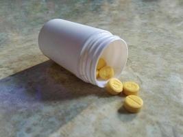 the yellow pills that comes out of a plastic medicine container. photo