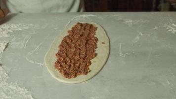 pita à la viande hachée. pita turc. préparation de pita avec de la viande hachée, femme mettant de la viande hachée et des saucisses sur de la pâte à pita. video