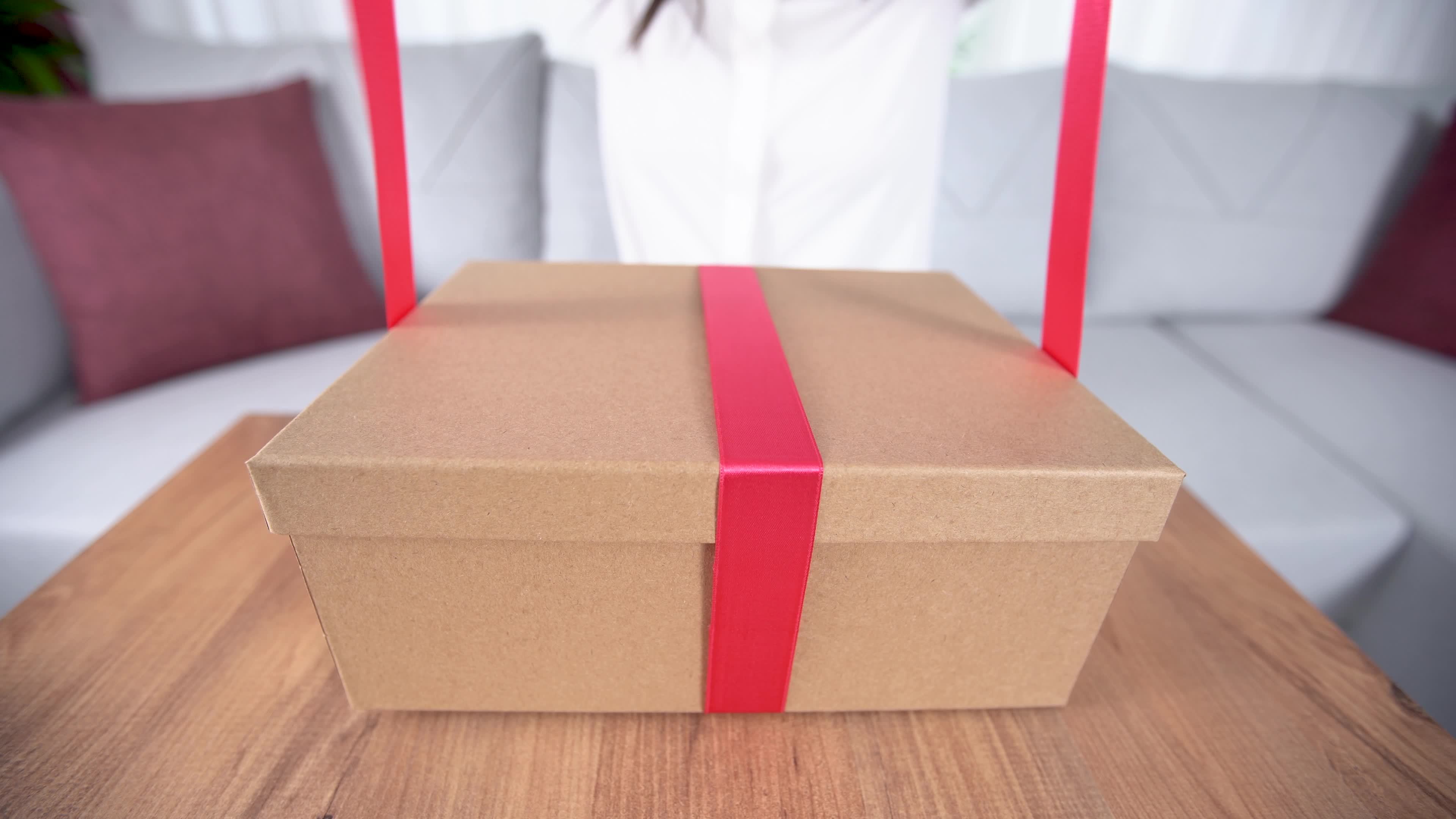 Making a gift box, tying it with a ribbon. The woman is tying the gift box with a ribbon
