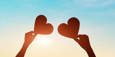 Silhouette of hands holding hearts on sunset sky background. love day concept photo