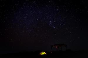 One yellow illiuminated tent stands by in the darkness by camping table wit stary magenta sky background photo