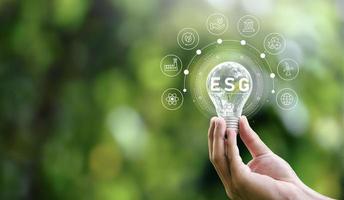 ESG icon concept in hand holding bulb for environmental, social and governance in sustainable and ethical business on networked connections on green background. photo