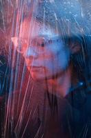 anteojos de plástico. foto de estudio en estudio oscuro con luz de neón. retrato de hombre serio detrás del vidrio mojado