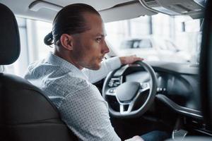 hombre probando auto nuevo en el salón durante el día. compra de vehiculo nuevo foto