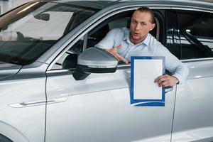 That's good deal, trust me. Manager sitting in modern white car with paper and documents in hands photo