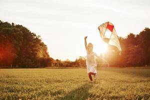 Positive kid. Happy girl in white clothes have fun with kite in the field. Beautiful nature photo