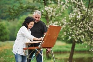 sonriendo y divirtiéndose. pareja madura tiene días libres y trabaja en la pintura juntos en el parque foto