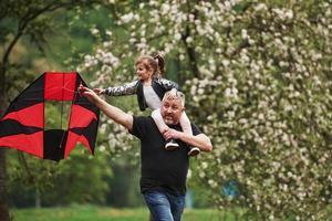 Running with red kite. Child sitting on the man's shoulders. Having fun photo