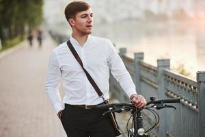 Focused photo. Businessman in formal clothes with black bicycle is in the city photo