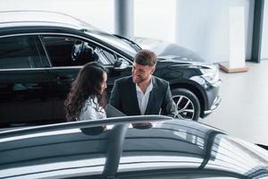 Charming young people. Female customer and modern stylish bearded businessman in the automobile saloon photo