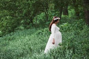 Enjoying nature. Beautiful pregnant woman in dress have a walk outdoors. Positive brunette photo