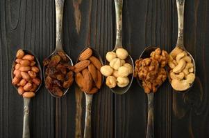Hazelnut, cashews, raisins, almonds, peanuts, walnuts in silver spoons on a rustic background photo