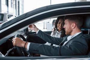 Active conversation. Lovely successful couple trying new car in the automobile salon photo