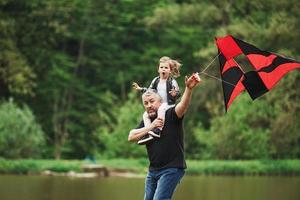 Like child again. Running with red kite. Kid sitting on the man's shoulders. Having fun photo