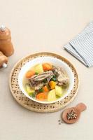 Sop Iga, Beef ribs soup, is Indonesian soup. Made from ribs, carrots, leeks, and potatoes. Served in white bowl. Selected focus photo