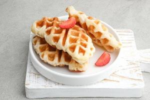 Plain Croissant Waffle or Croffle served in white plate with strawberry and mint leaf topping. photo