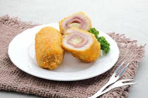 cordon blue crujiente, rollo de filete de pollo con jamón y queso. servido en plato blanco sobre fondo gris. foto
