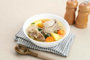 Sop Iga, Beef ribs soup, is Indonesian soup. Made from ribs, carrots, leeks, and potatoes. Served in white bowl. Selected focus photo
