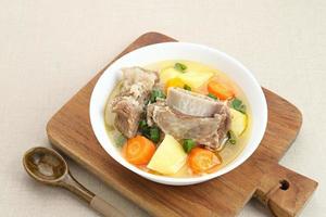 Sop Iga, Beef ribs soup, is Indonesian soup. Made from ribs, carrots, leeks, and potatoes. Served in white bowl. Selected focus photo