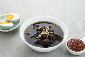Rawon, Indonesian Traditional beef black soup. Served on a bowl with mung bean sprouts, chilli paste and salted egg photo