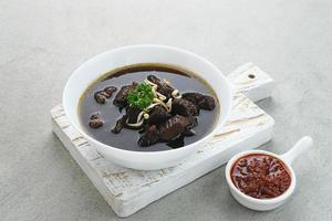 Rawon, Indonesian Traditional beef black soup. Served on a bowl with mung bean sprouts, chilli paste and salted egg photo