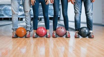 sosteniendo pelotas por las piernas. vista recortada de la gente en el club de bolos lista para divertirse foto