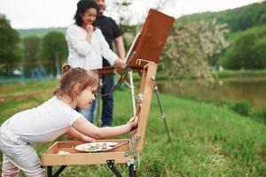 In white shirt. Grandmother and grandfather have fun outdoors with granddaughter. Painting conception photo