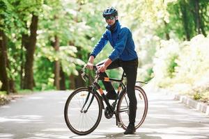 buen clima hoy. ciclista en bicicleta está en la carretera asfaltada en el bosque en un día soleado foto