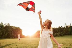 Woman is far away. Mother and daughter have fun with kite in the field. Beautiful nature photo