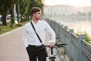 Such a lovely weather. Businessman in formal clothes with black bicycle is in the city photo