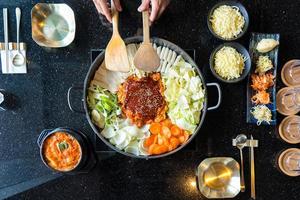 Tokboki Korean traditional food hot and spicy rice cake, combination and apply puff with cheese and vegetable on the black table photo