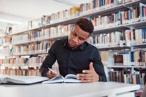 estudiante inteligente hombre afroamericano sentado en la biblioteca y buscando información en los libros foto